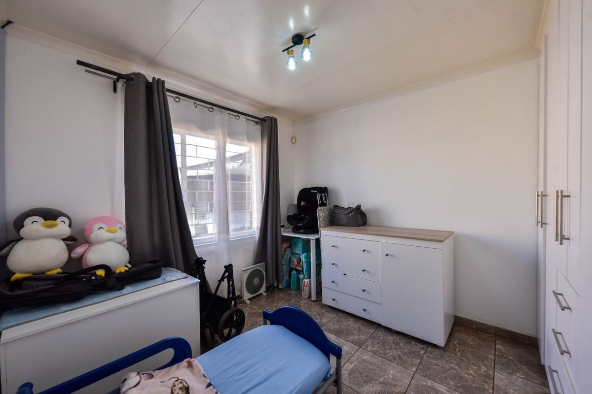 A bedroom featuring tiled flooring, built-in cupboards, and a window with security bars.