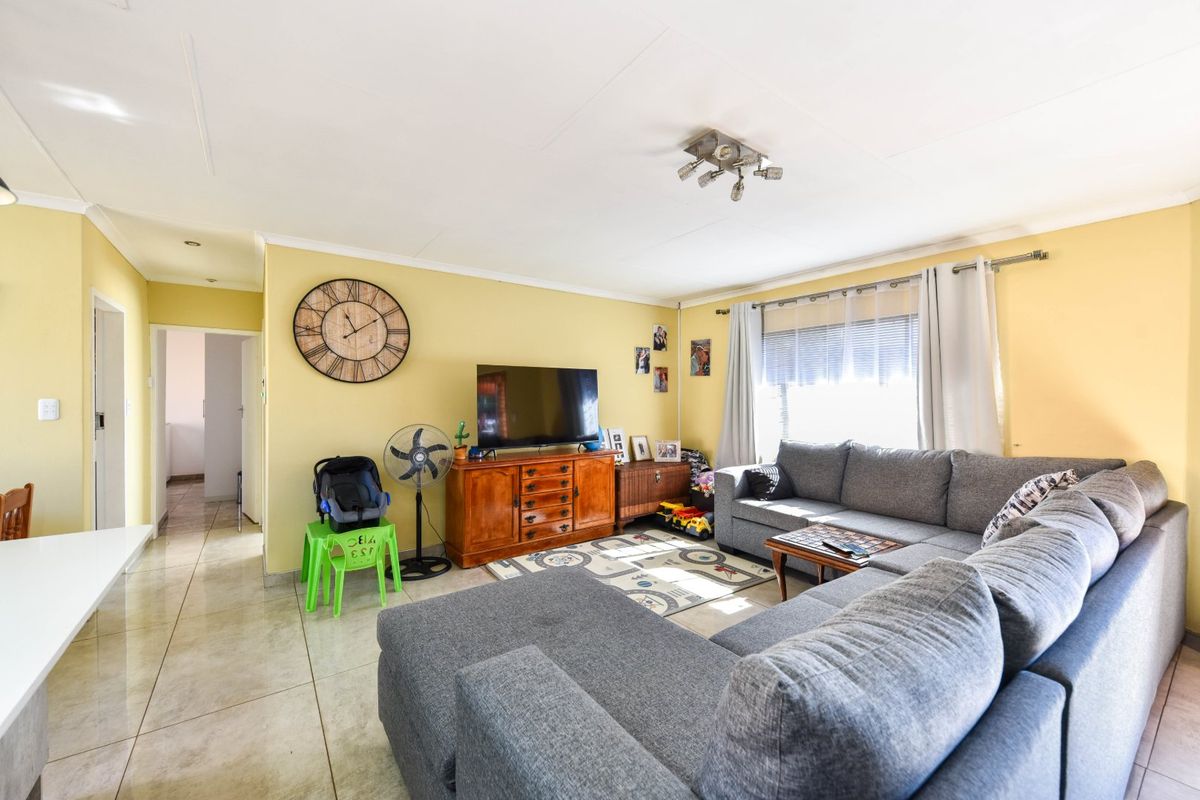 A spacious living room featuring tiled flooring, neutral yellow walls, and large windows allowing for natural light.