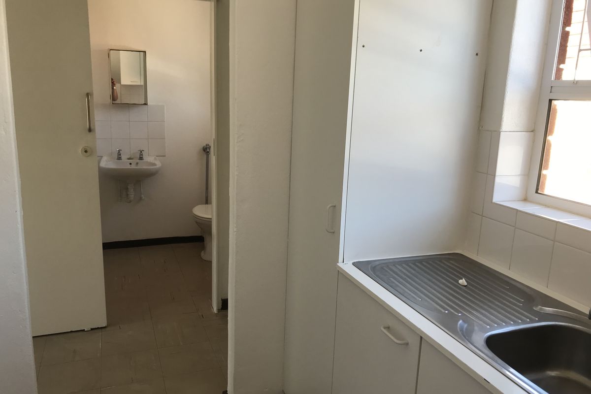 A functional kitchen area featuring built-in cabinetry and a stainless steel sink, with an adjacent small bathroom containing a toilet and pedestal basin.