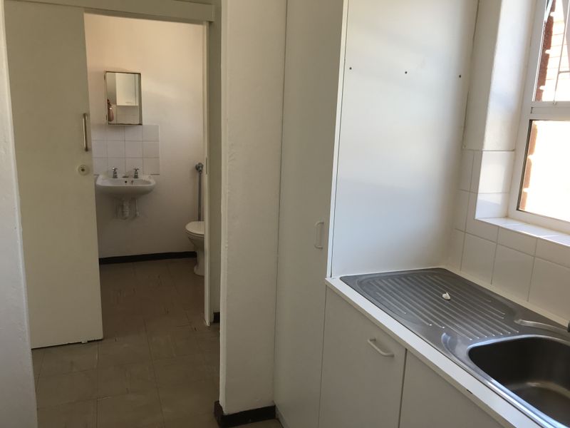 A functional kitchen area featuring built-in cabinetry and a stainless steel sink, with an adjacent small bathroom containing a toilet and pedestal basin.