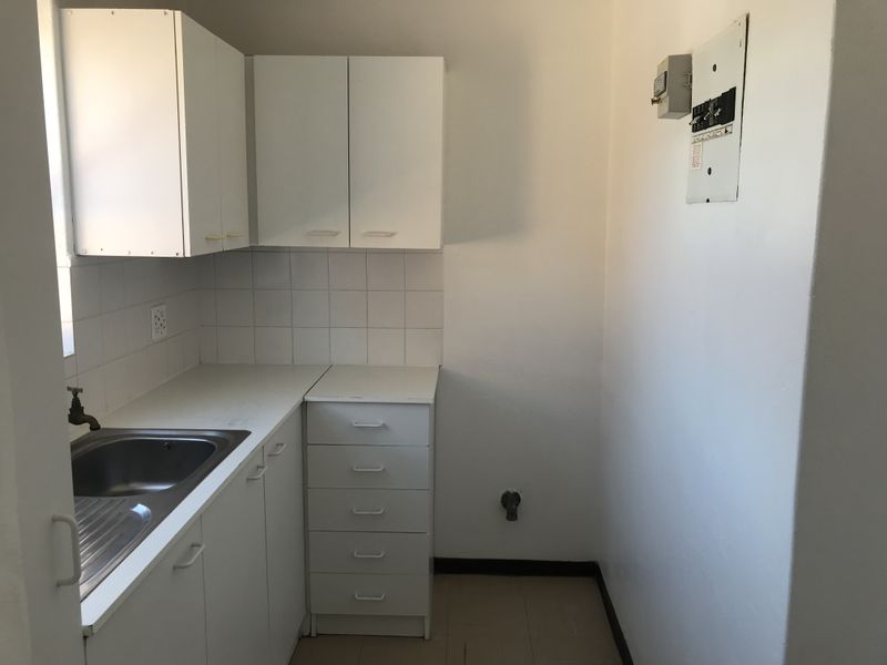 A functional laundry area featuring built-in white cabinetry, a stainless steel sink, and a wall-mounted electrical distribution board.