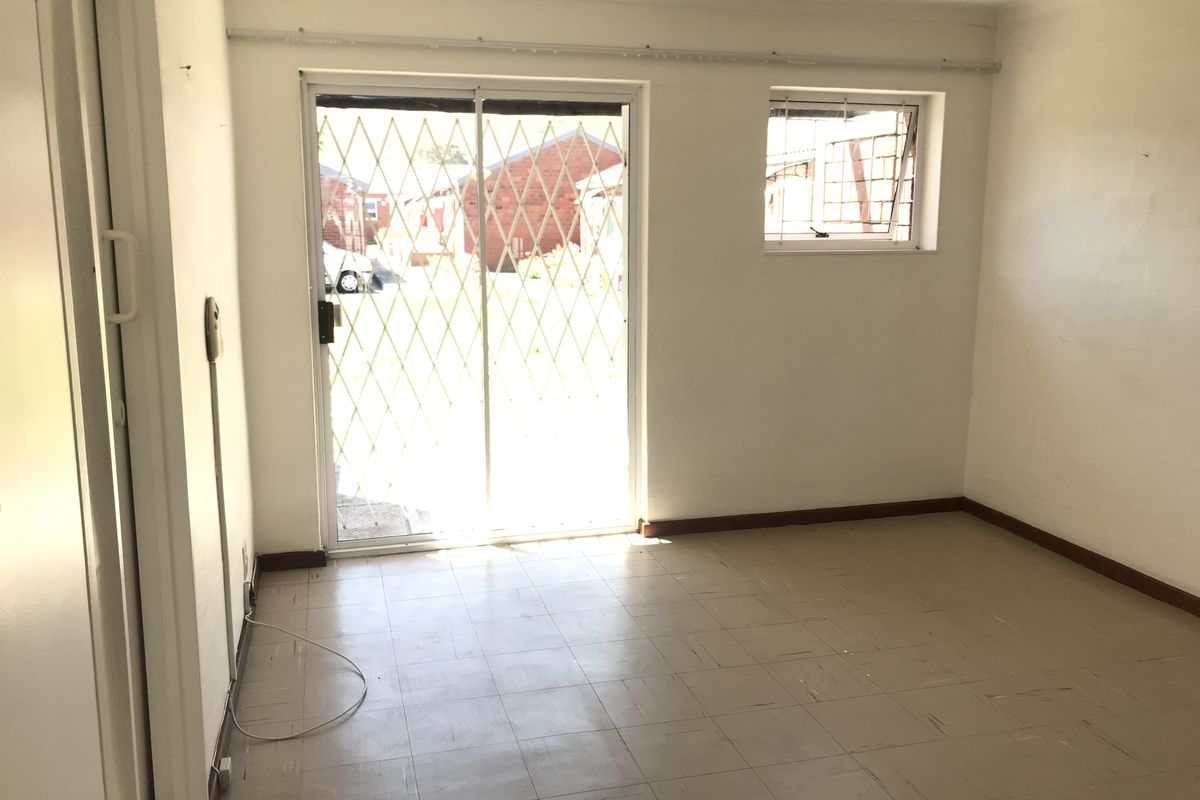 An empty living room featuring tiled flooring, a sliding glass door with a security gate, and a window with security bars.