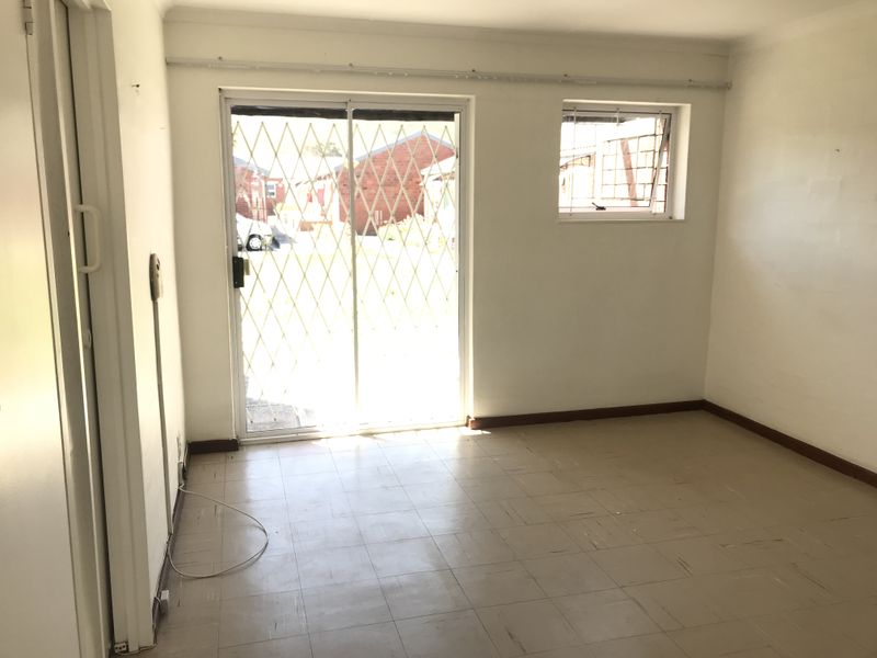 An empty living room featuring tiled flooring, a sliding glass door with a security gate, and a window with security bars.