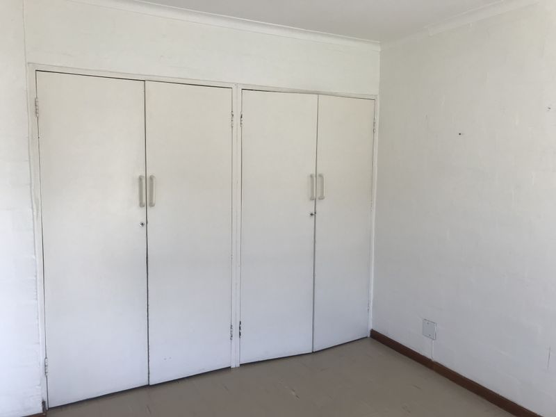 An empty bedroom featuring built-in cupboards with white doors and simple skirting boards, presenting a blank canvas for potential interior updates.