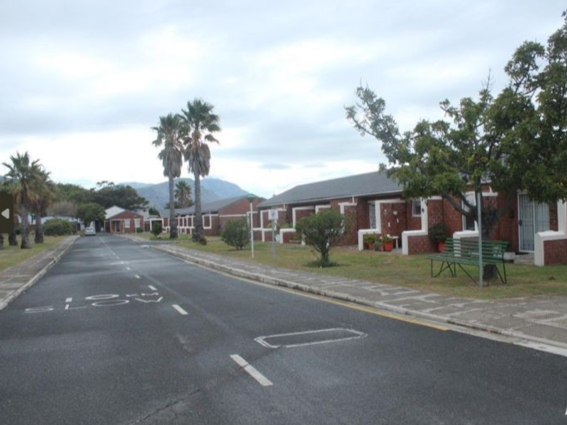 A street view of a townhouse complex featuring brick-faced units, paved walkways, and established landscaping under an overcast sky.