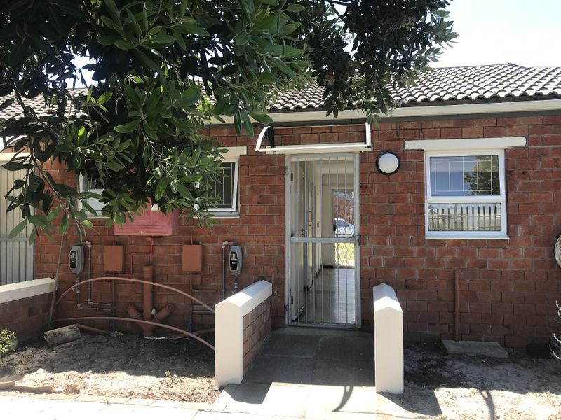 Front entrance of a brick townhouse featuring a security gate, tiled roof, and visible external utility infrastructure.