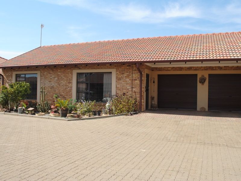Front elevation of a retirement village unit featuring a brick facade, tiled roof, and a double garage with a paved driveway.