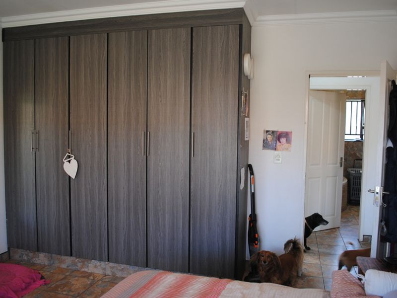 A bedroom featuring a large, modern wood-grain built-in wardrobe and tiled flooring, with an adjoining doorway leading to another room.