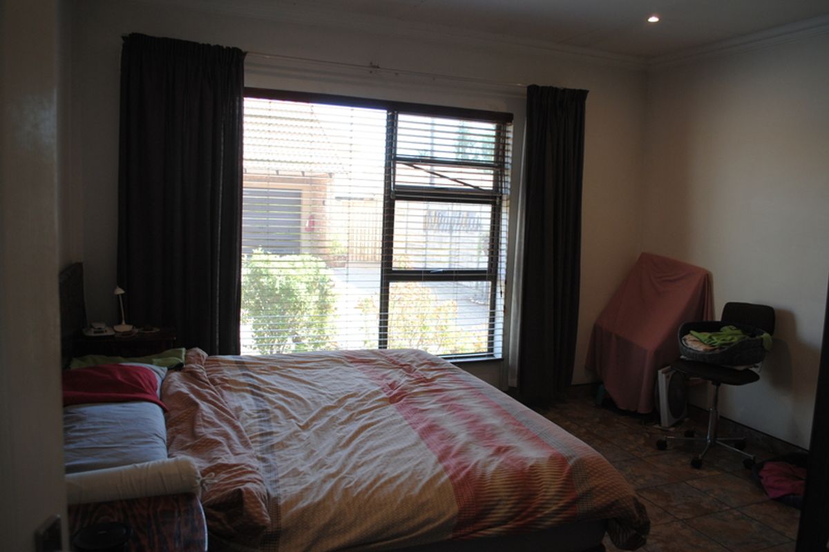 A bedroom featuring tiled flooring, recessed downlighting, and a large window with venetian blinds, offering a functional space for rest.