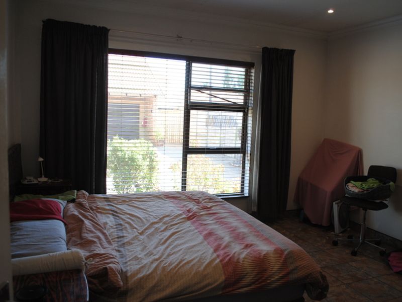 A bedroom featuring tiled flooring, recessed downlighting, and a large window with venetian blinds, offering a functional space for rest.