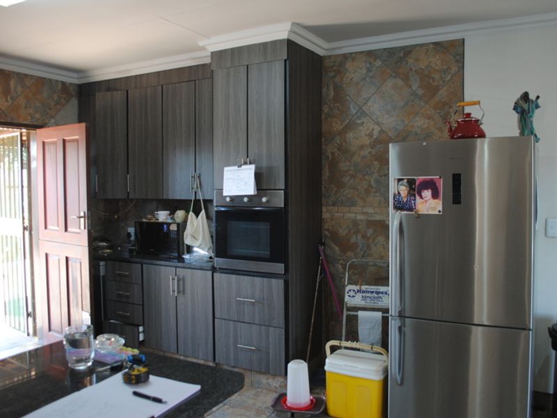A functional kitchen featuring dark wood-grain cabinetry, granite countertops, and decorative stone-look wall tiling with direct access to an outdoor area.