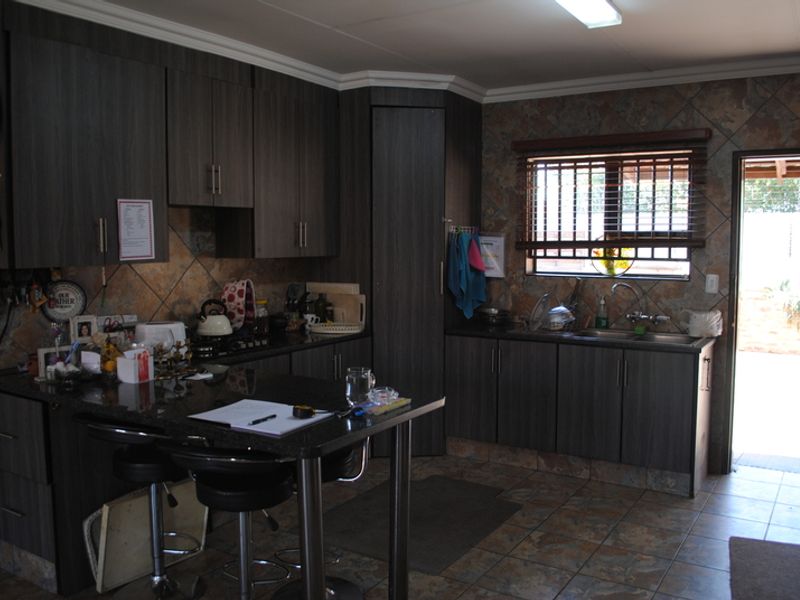 A functional kitchen featuring dark wood cabinetry, granite countertops, a double bowl sink, and tiled finishes with direct access to the exterior.