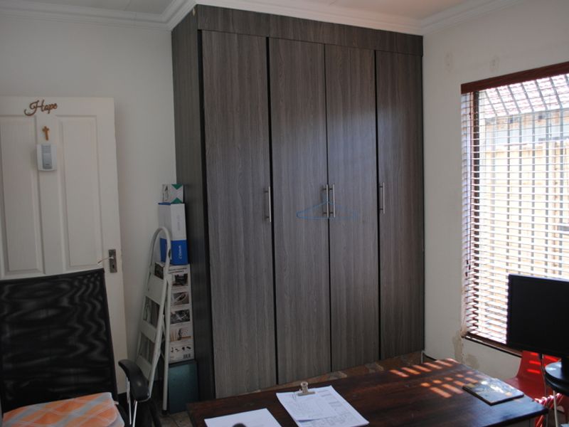 Bedroom featuring a dark wood-grain built-in wardrobe, venetian blinds, and security bars on the window.