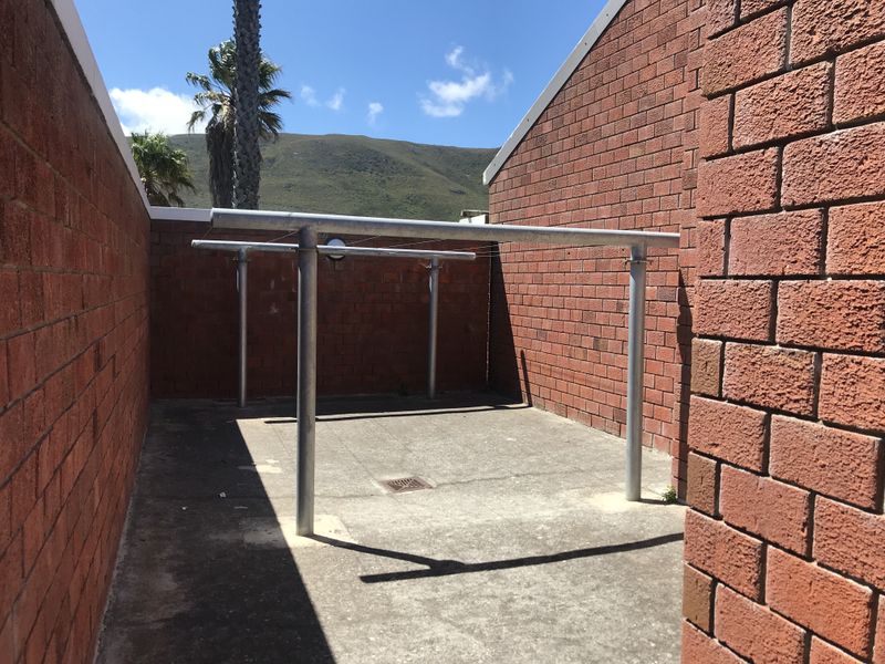 An outdoor utility or drying area featuring exposed brick walls, concrete flooring, and a fixed metal washing line structure.