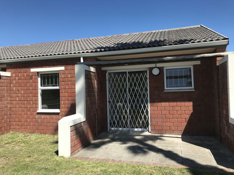 A well-maintained rear exterior view featuring a brick facade, concrete tile roof, paved patio area, and a secure metal gate entrance.