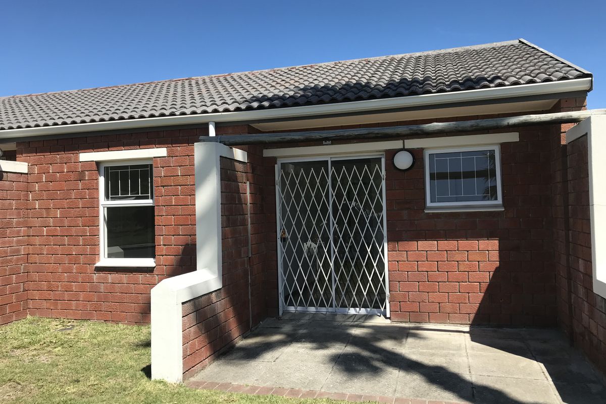 A well-maintained rear exterior view featuring a brick facade, concrete tile roof, paved patio area, and a secure metal gate entrance.