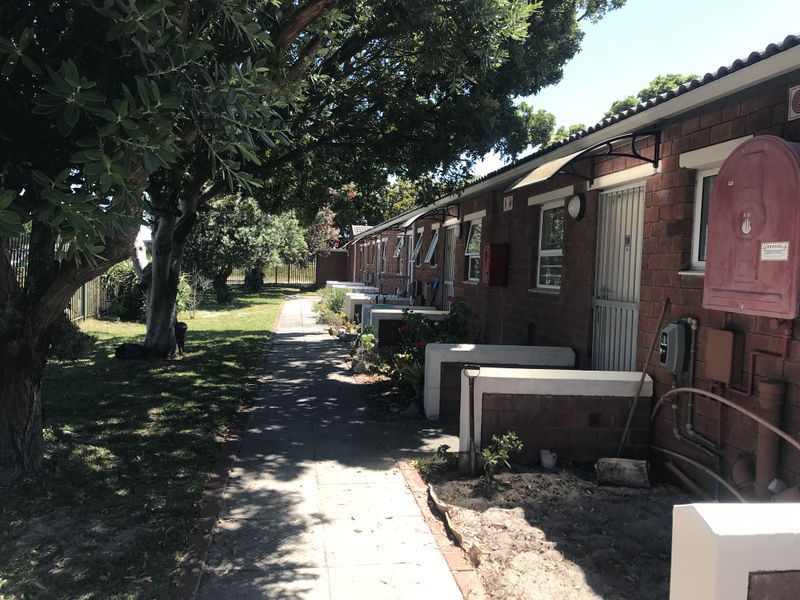 A view of the rear exterior of the property featuring a brick facade, paved walkway, and established garden area.