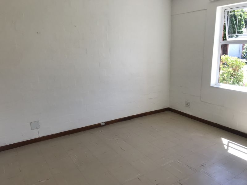 An empty bedroom featuring painted brick walls, vinyl tile flooring, and a casement window with natural light.