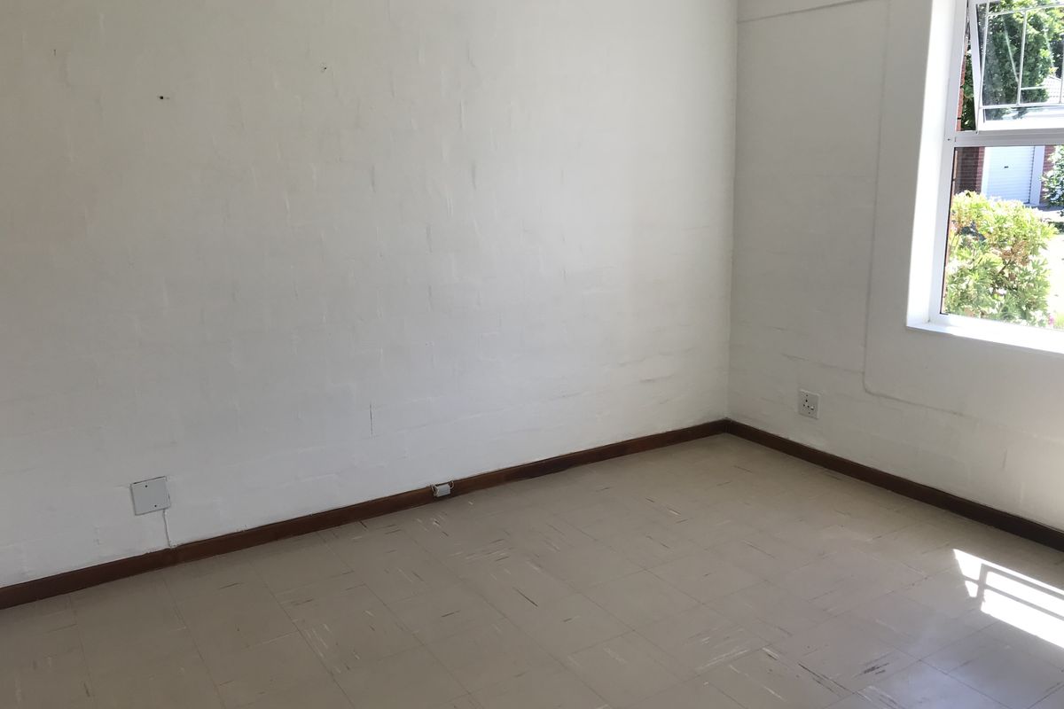 An empty bedroom featuring painted brick walls, vinyl tile flooring, and a casement window with natural light.