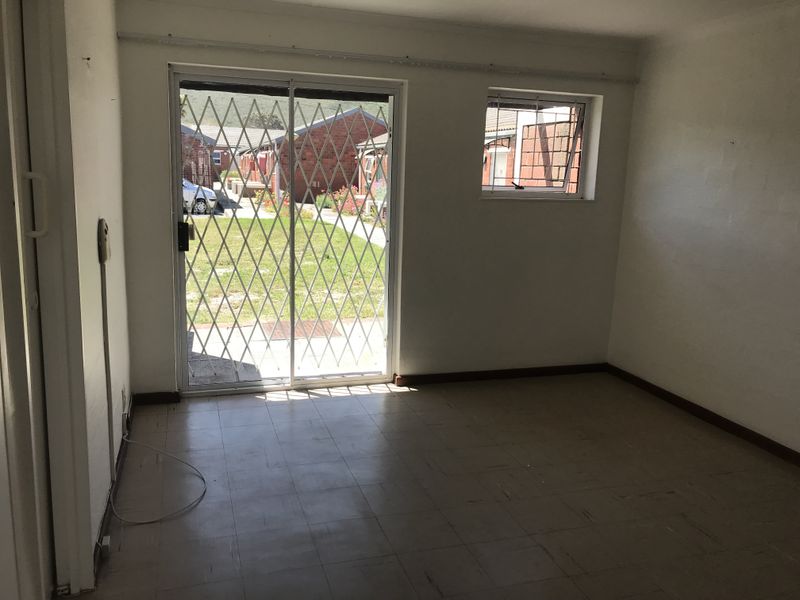 An empty living room featuring tiled flooring, a sliding glass door with a security gate, and a window with security bars.