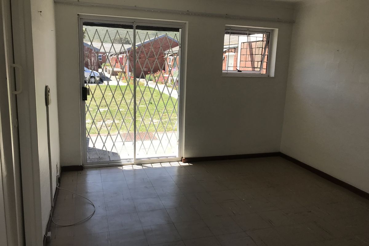 An empty living room featuring tiled flooring, a sliding glass door with a security gate, and a window with security bars.