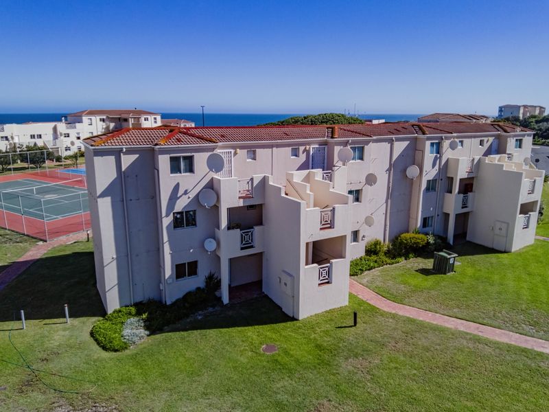 Aerial view of a multi-story apartment complex featuring terracotta roofing, private balconies, and access to communal recreational facilities including a tennis court.