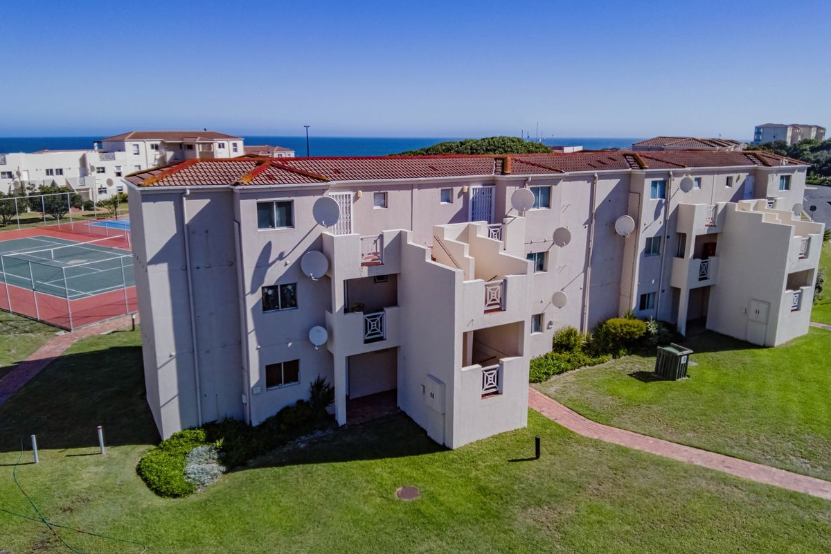Aerial view of a multi-story apartment complex featuring terracotta roofing, private balconies, and access to communal recreational facilities including a tennis court.
