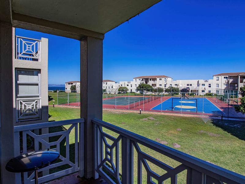 A covered balcony overlooking a communal garden area featuring a tennis court and basketball court within the apartment complex.