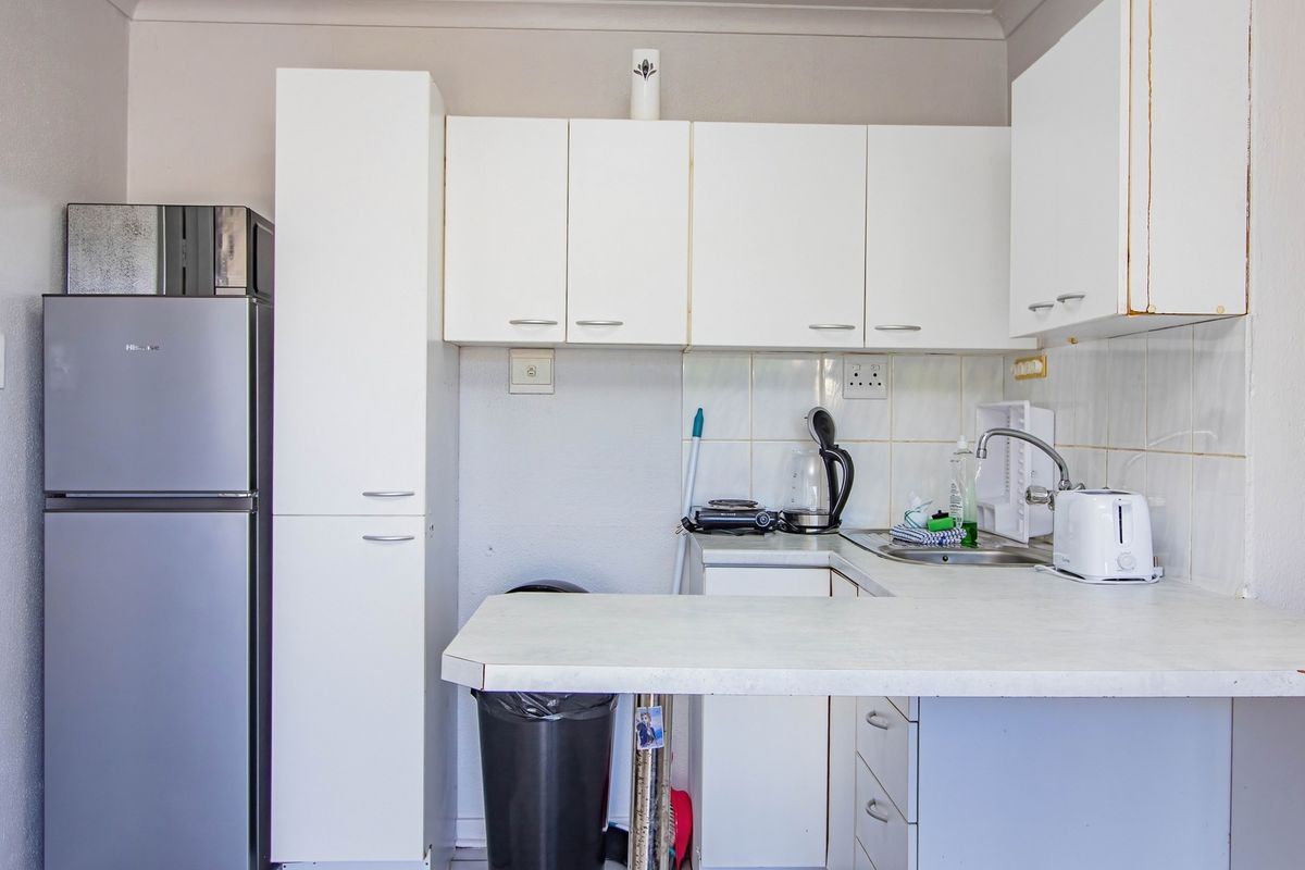 A compact kitchen featuring white cabinetry, a laminate countertop, and a stainless steel sink with a tiled backsplash.