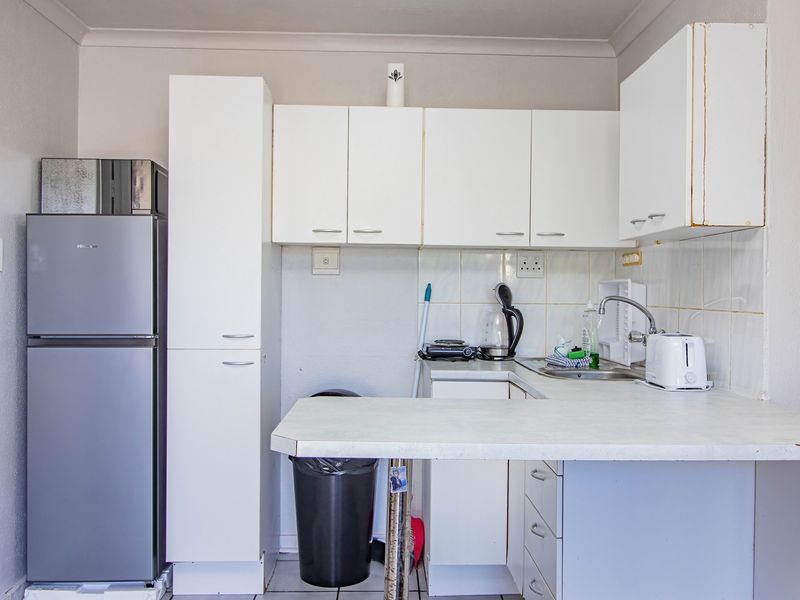 A compact kitchen featuring white cabinetry, a laminate countertop, and a stainless steel sink with a tiled backsplash.