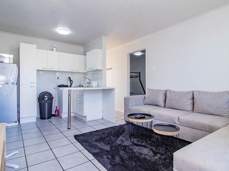 Open plan living area featuring tiled flooring and a compact kitchen with built-in cabinetry, seamlessly connecting to the lounge space.
