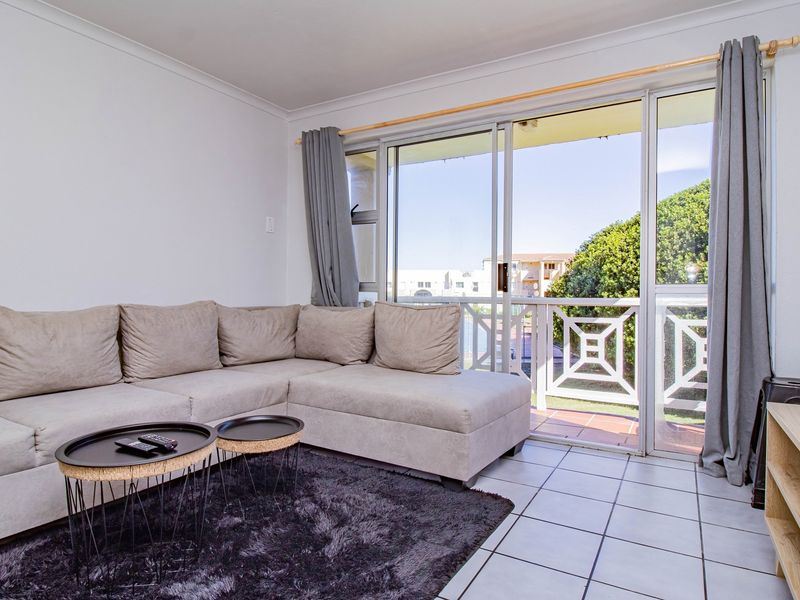 A bright living room featuring tiled flooring and large sliding glass doors that provide access to an outdoor balcony area.
