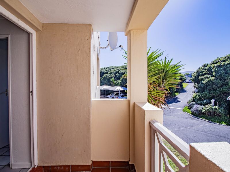 A covered balcony area featuring tiled flooring and a balustrade, offering an elevated view of the surrounding complex grounds.
