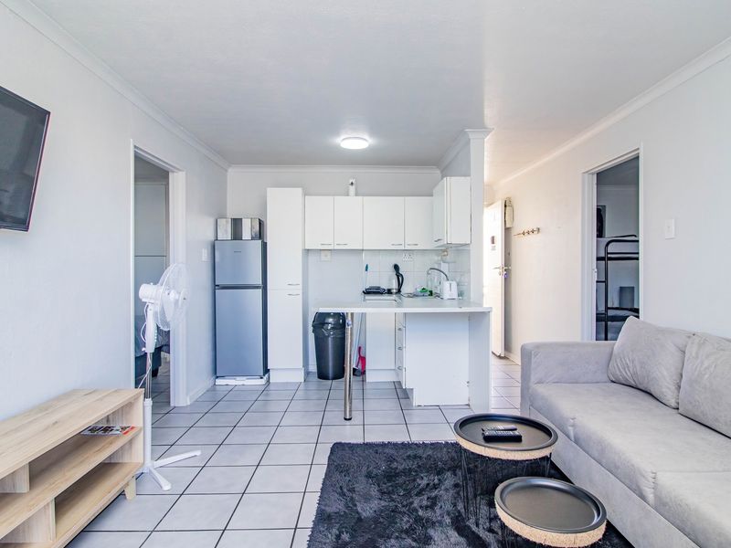 Open-plan living area featuring a compact kitchen with white cabinetry, a breakfast counter, and tiled flooring throughout the space.