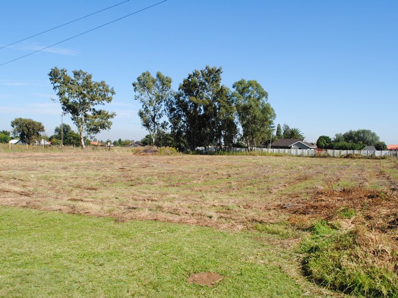 A vacant residential plot featuring cleared grass, mature trees, and perimeter wire fencing, offering a blank canvas for future development.