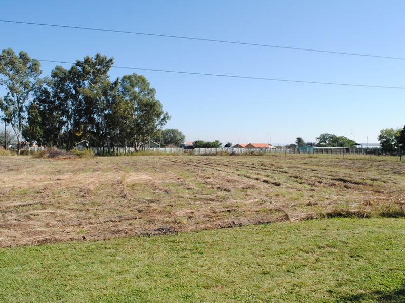A wide, open residential plot featuring cleared grass, mature trees, and perimeter fencing, offering a blank canvas for future development.