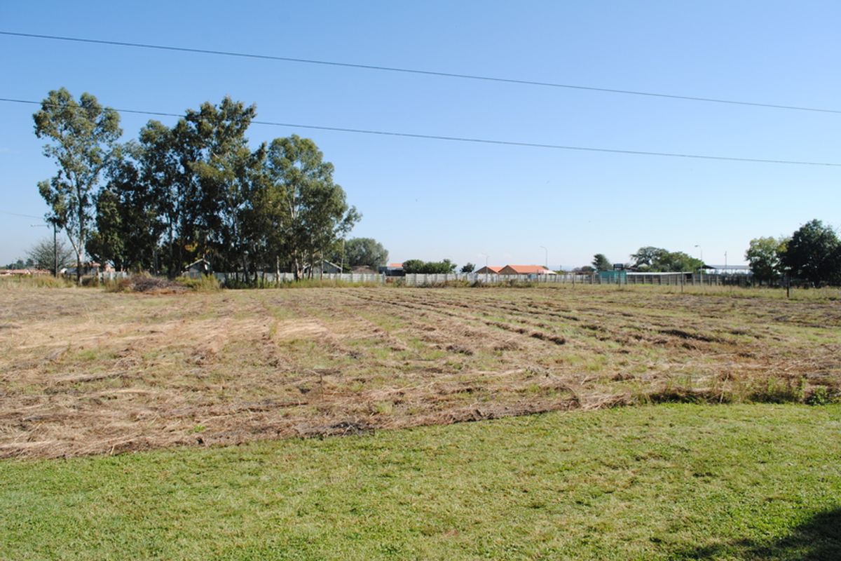 A wide, open residential plot featuring cleared grass, mature trees, and perimeter fencing, offering a blank canvas for future development.