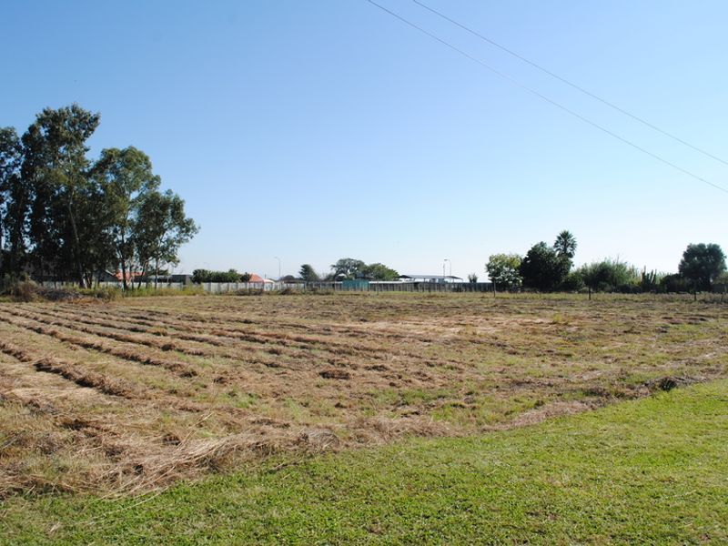 A wide-angle view of a vacant residential plot featuring cleared land and perimeter fencing under a clear blue sky.