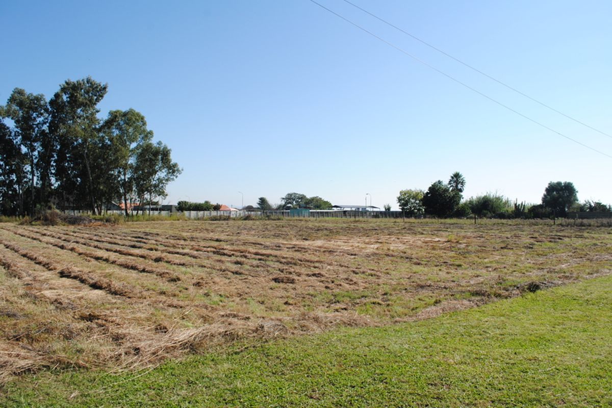 A wide-angle view of a vacant residential plot featuring cleared land and perimeter fencing under a clear blue sky.