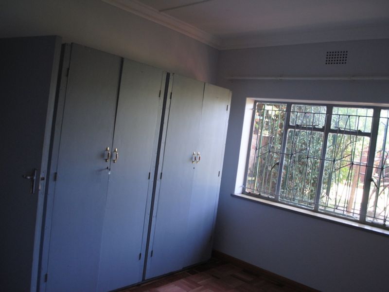 A vacant bedroom featuring built-in cupboards, parquet flooring, and a window fitted with security bars.