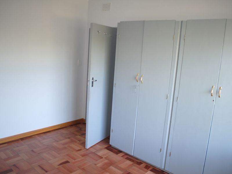 A vacant bedroom featuring classic parquet flooring and built-in cupboards with painted finishes.