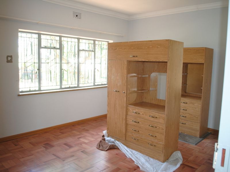 A bedroom featuring parquet flooring, large windows with security bars, and built-in wooden cabinetry.