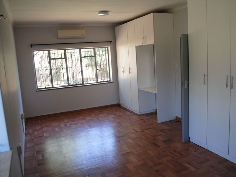 Spacious bedroom featuring polished parquet flooring, extensive built-in cabinetry, and an integrated air conditioning unit.