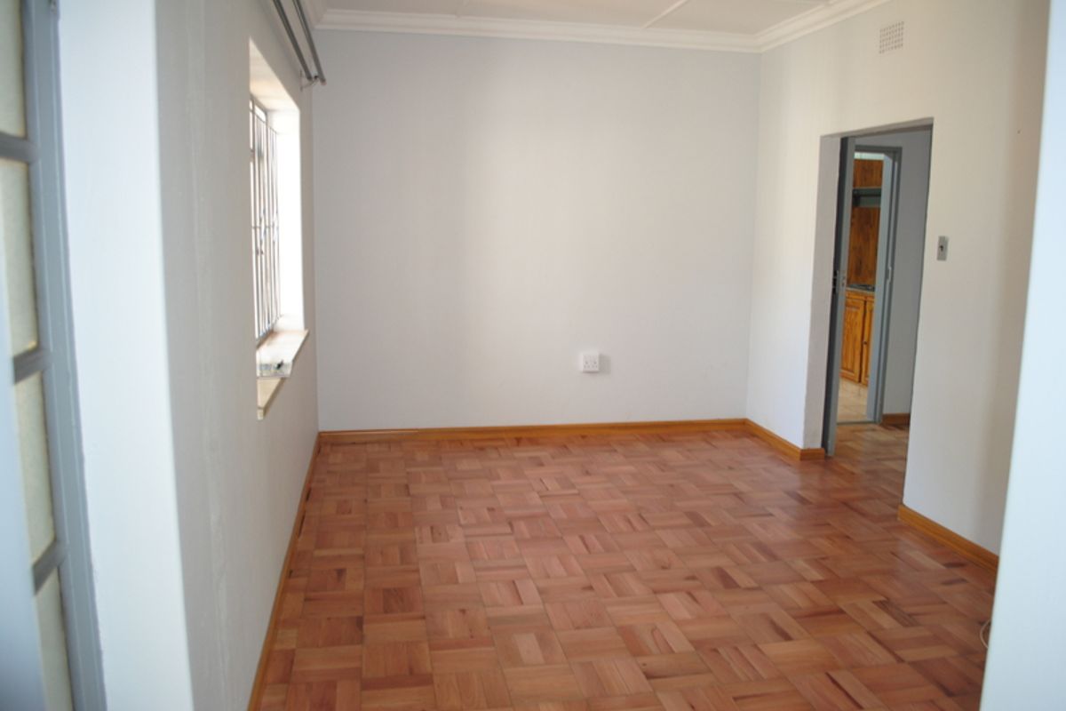 A bright, empty bedroom featuring well-maintained parquet flooring, neutral walls, and security bars on the window.