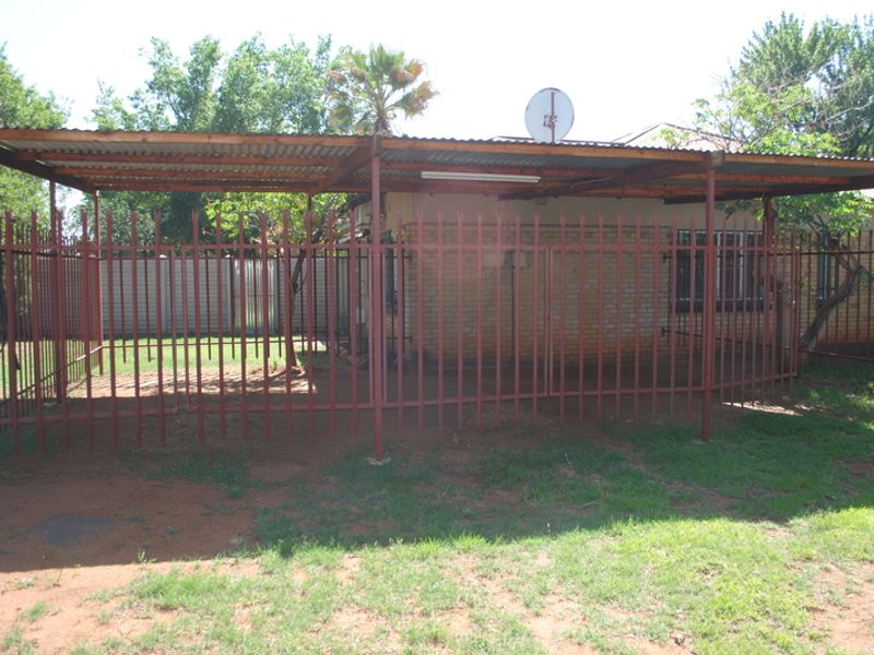 Rear exterior view showing a covered patio area with a corrugated metal roof, steel support structure, and perimeter security fencing.