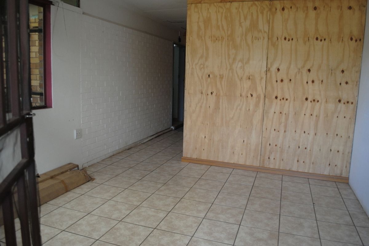 An empty living area featuring tiled flooring and a prominent plywood partition wall, requiring cosmetic updates to improve the overall aesthetic.