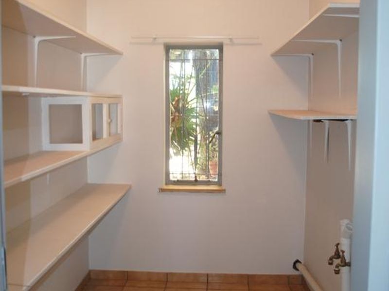 A functional scullery or pantry area featuring built-in shelving, tiled flooring, and dedicated plumbing connections for utility use.