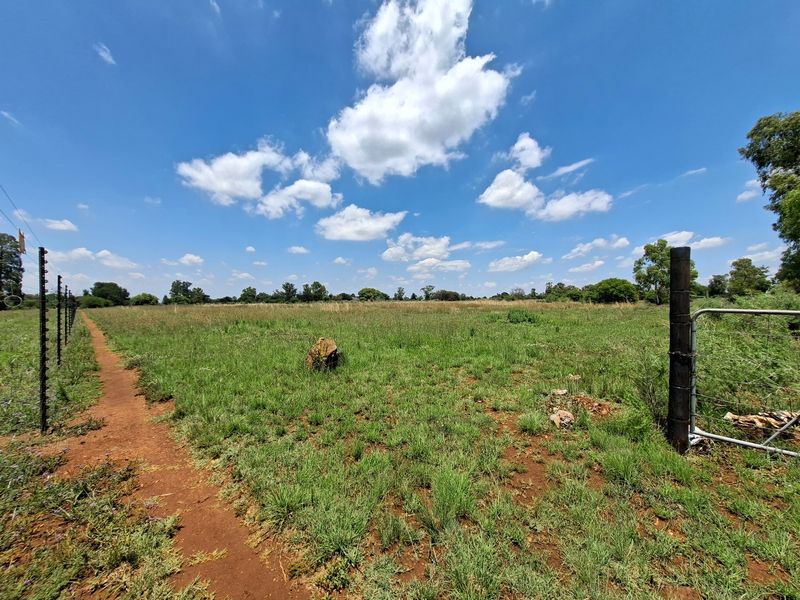 A view of a vacant residential plot featuring established perimeter fencing and a metal gate entrance.
