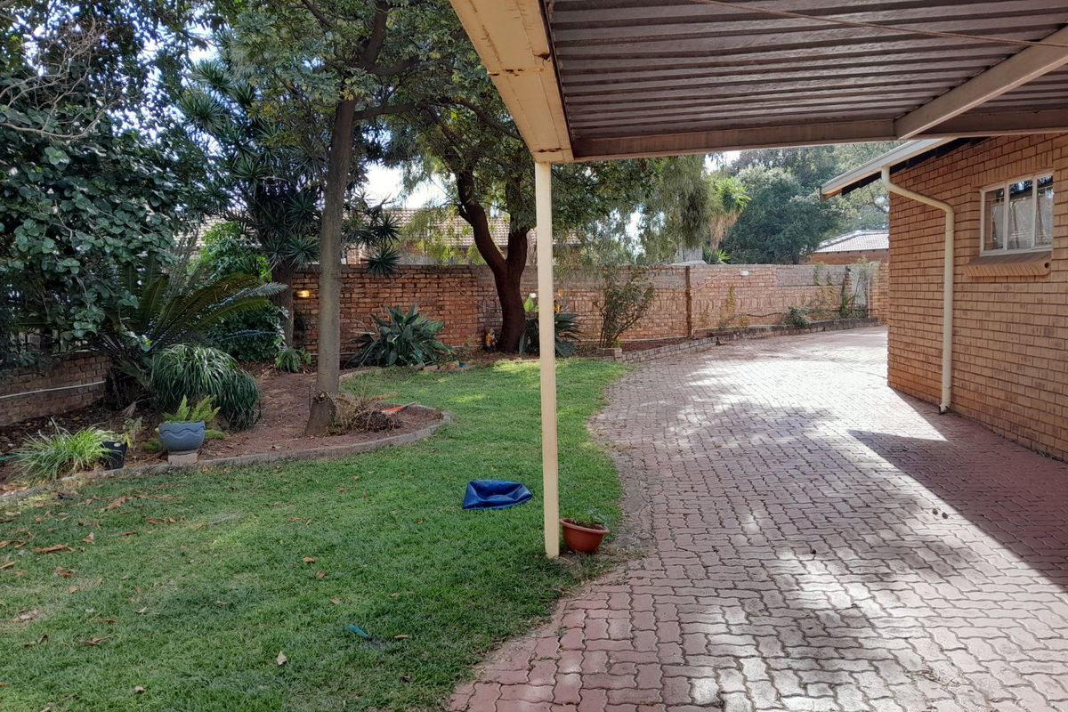A view of the side garden and paved driveway area featuring a covered carport structure and established trees.
