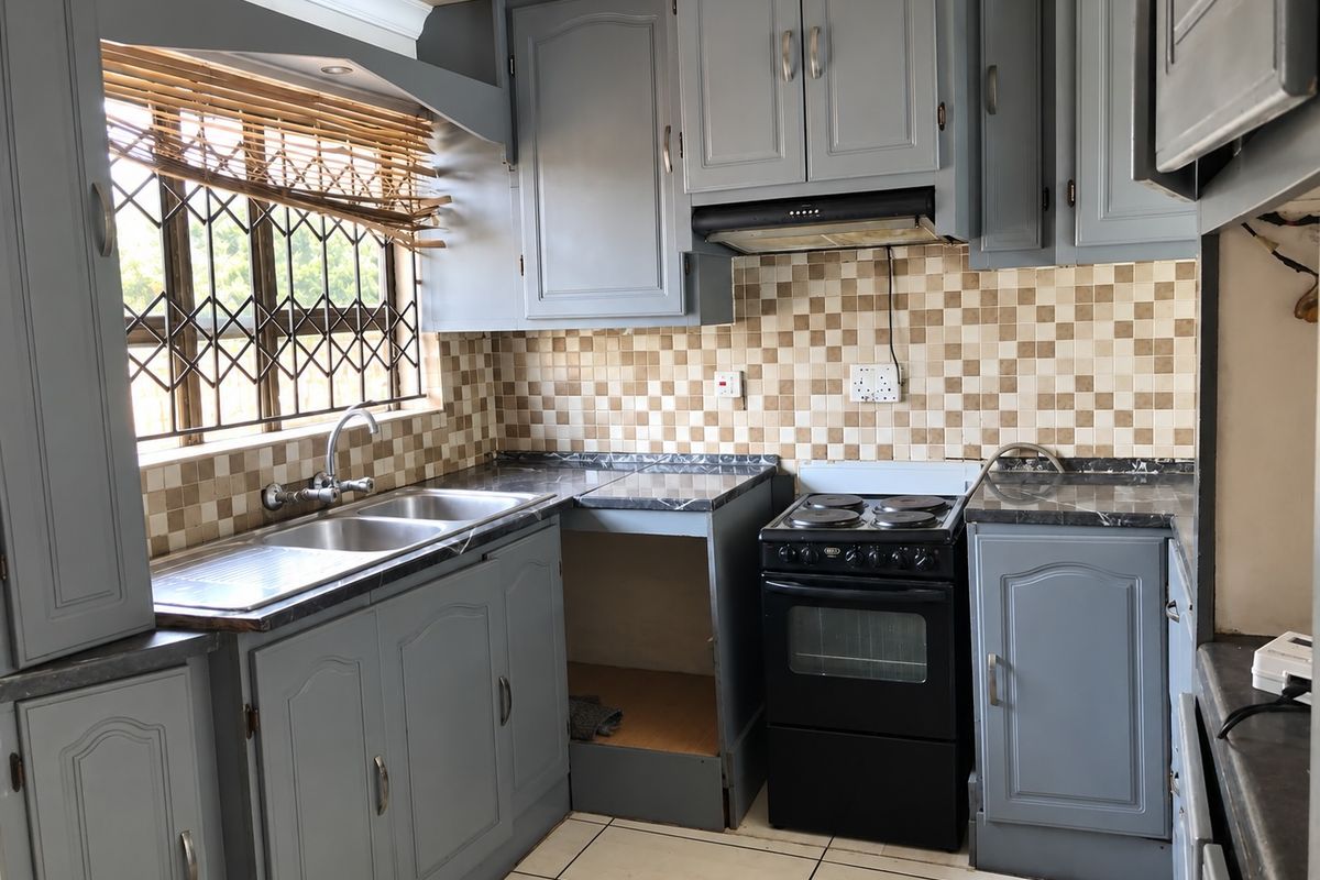 A functional kitchen featuring grey cabinetry, a double bowl sink, tiled backsplash, and a freestanding stove with an integrated extractor fan.